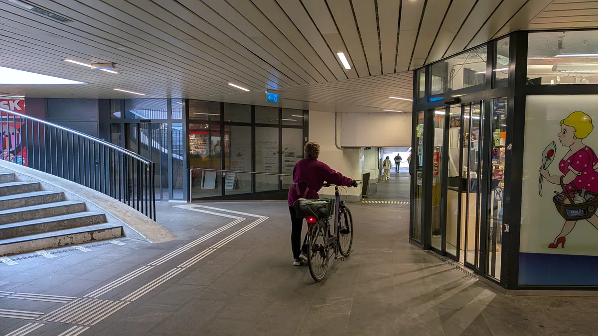 Man sieht eine düstere Bahnhofunterführung mit Passanten und Velofahrern.